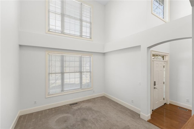 empty room featuring arched walkways, a towering ceiling, visible vents, baseboards, and carpet