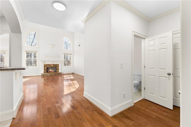 interior space with baseboards, a lit fireplace, wood-type flooring, and crown molding