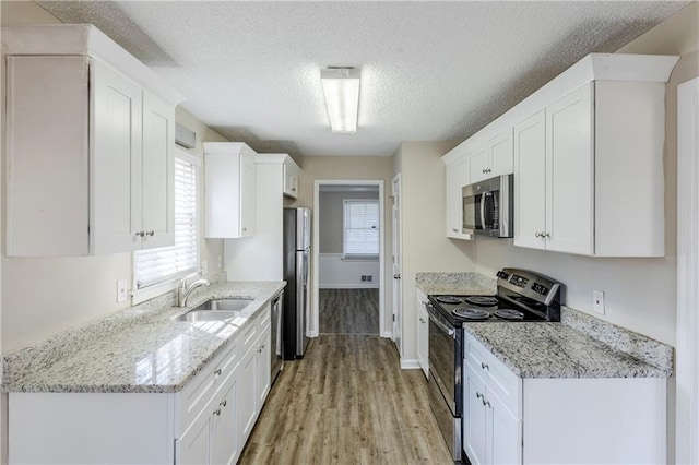 kitchen with white cabinets, appliances with stainless steel finishes, sink, and light stone counters