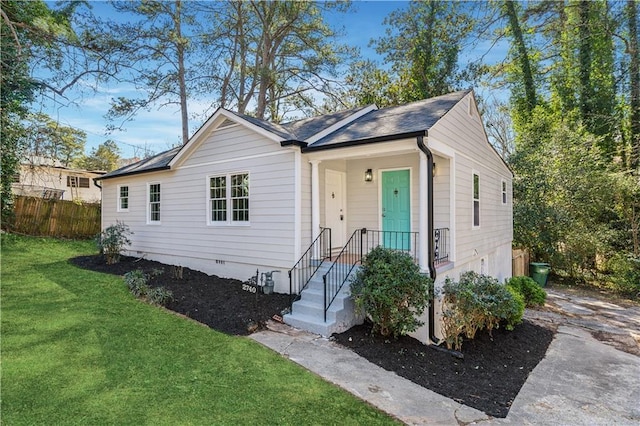 view of front facade with a front yard, crawl space, roof with shingles, and fence