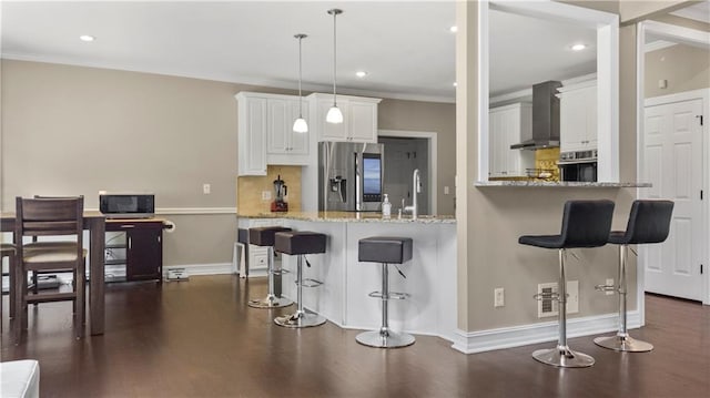 kitchen featuring wall chimney range hood, appliances with stainless steel finishes, a kitchen bar, and dark wood-type flooring