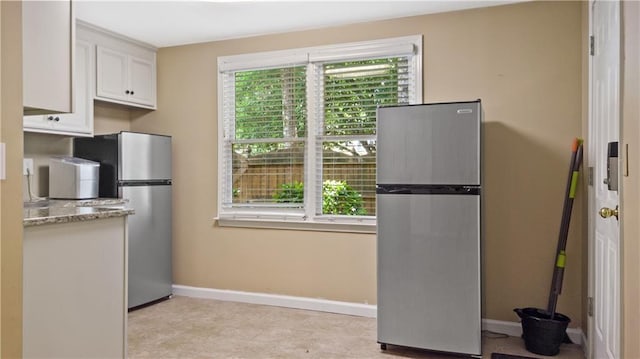 kitchen featuring baseboards, freestanding refrigerator, white cabinetry, and light stone counters