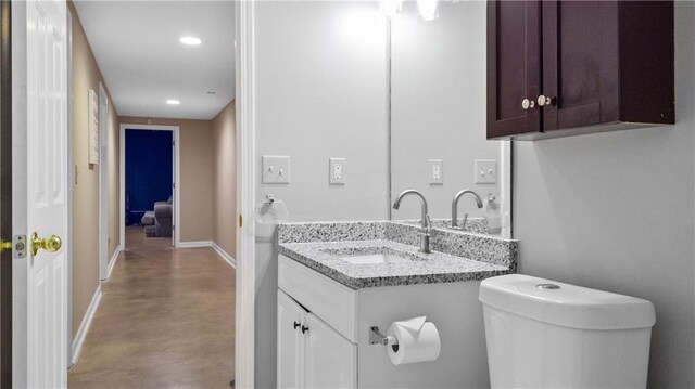 half bathroom with concrete flooring, baseboards, vanity, toilet, and recessed lighting