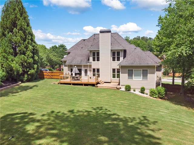 back of house featuring a shingled roof, a deck, a chimney, a lawn, and fence private yard