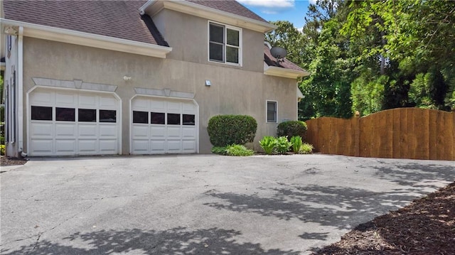 view of side of property featuring aphalt driveway, roof with shingles, and stucco siding