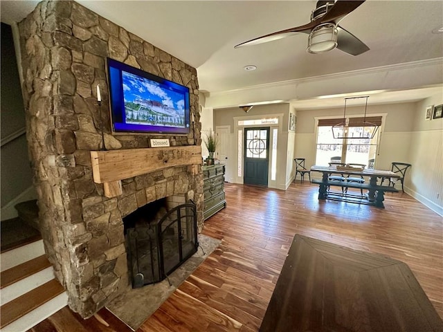 living room featuring ornamental molding, a stone fireplace, hardwood / wood-style flooring, and ceiling fan