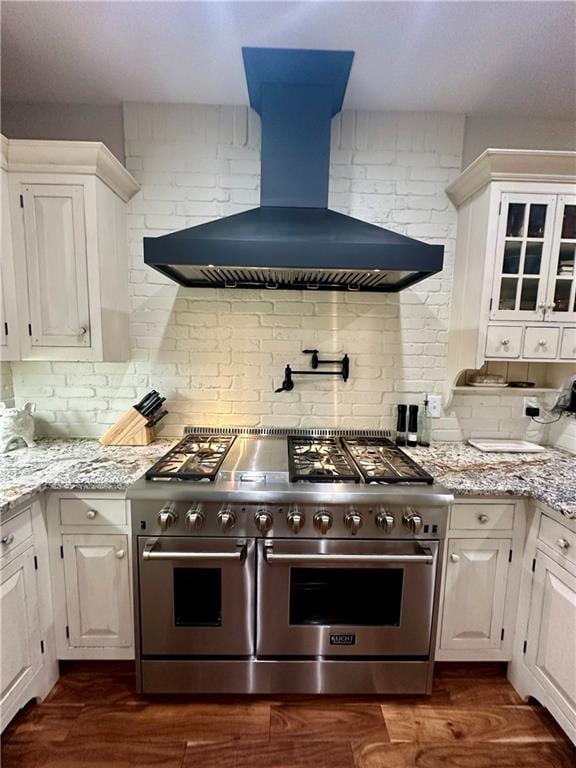 kitchen featuring range with two ovens, white cabinetry, custom exhaust hood, light stone counters, and decorative backsplash