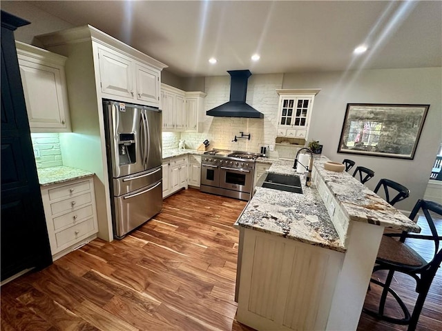 kitchen featuring wall chimney range hood, a kitchen bar, dark wood-type flooring, sink, and stainless steel appliances