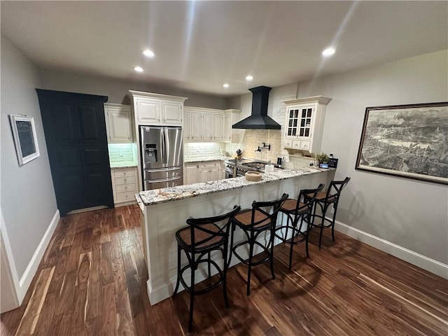 kitchen featuring wall chimney range hood, dark hardwood / wood-style flooring, kitchen peninsula, a kitchen breakfast bar, and stainless steel fridge with ice dispenser