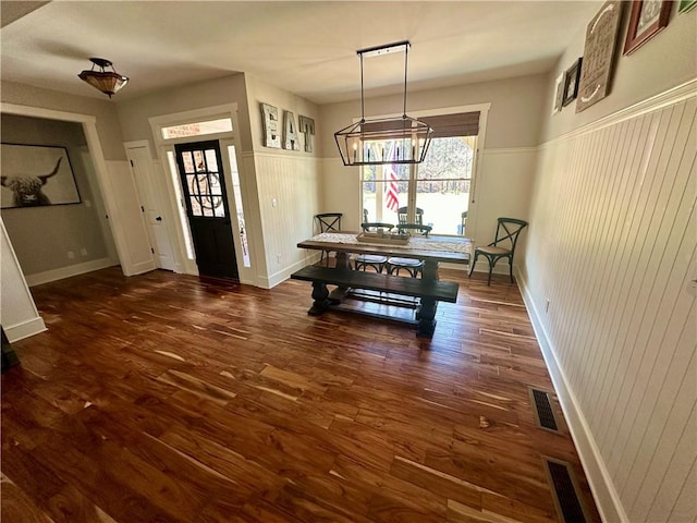 dining space with dark wood-type flooring, a notable chandelier, and wooden walls