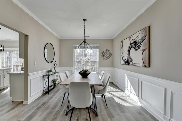 dining area featuring a wealth of natural light, light wood finished floors, a notable chandelier, and a wainscoted wall