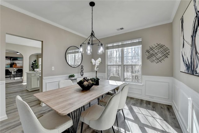 dining room with arched walkways, crown molding, visible vents, light wood-style flooring, and wainscoting