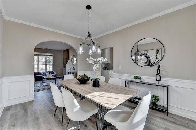 dining space featuring arched walkways, ornamental molding, wainscoting, and light wood-style flooring