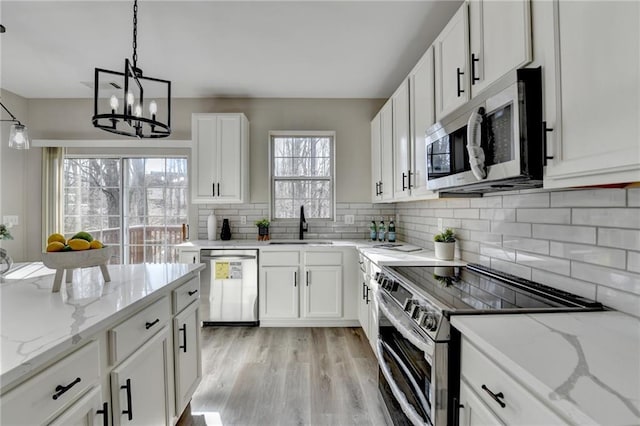 kitchen featuring light wood finished floors, tasteful backsplash, appliances with stainless steel finishes, white cabinetry, and a sink