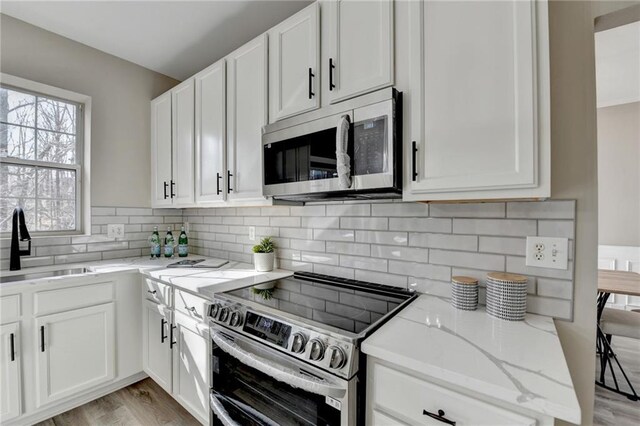 kitchen featuring tasteful backsplash, white cabinets, appliances with stainless steel finishes, light stone countertops, and a sink