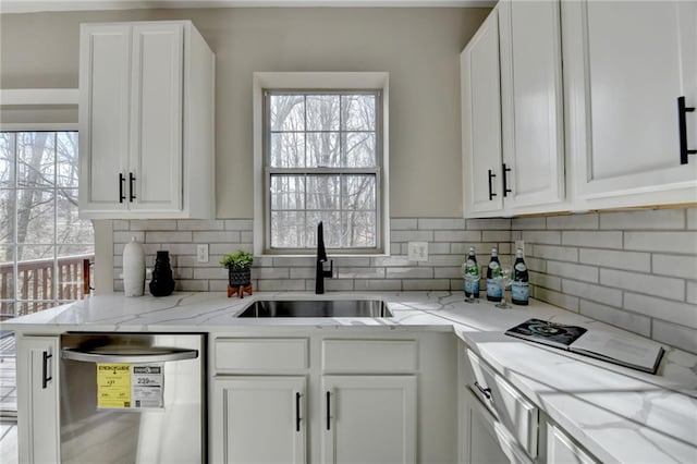 kitchen with light stone counters, decorative backsplash, white cabinets, a sink, and dishwasher