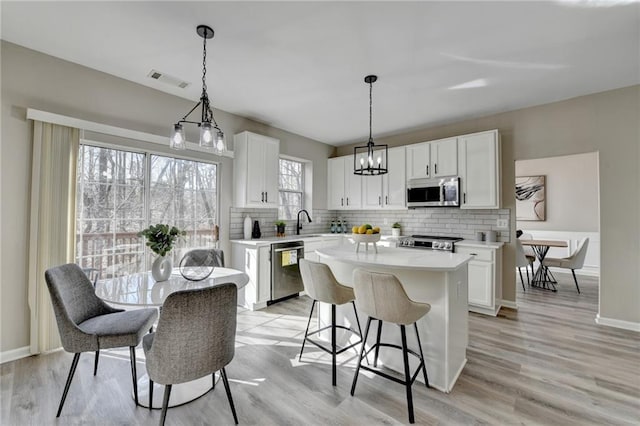 kitchen featuring stainless steel appliances, a kitchen island, white cabinetry, light countertops, and decorative backsplash