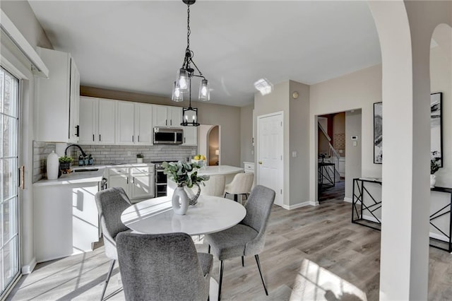 dining space featuring light wood finished floors, baseboards, and arched walkways