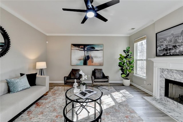 living room featuring baseboards, a ceiling fan, wood finished floors, crown molding, and a high end fireplace