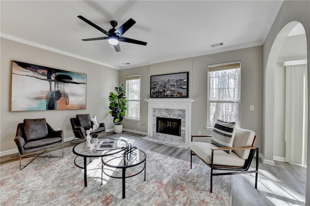 living room with a high end fireplace, wood finished floors, visible vents, and crown molding