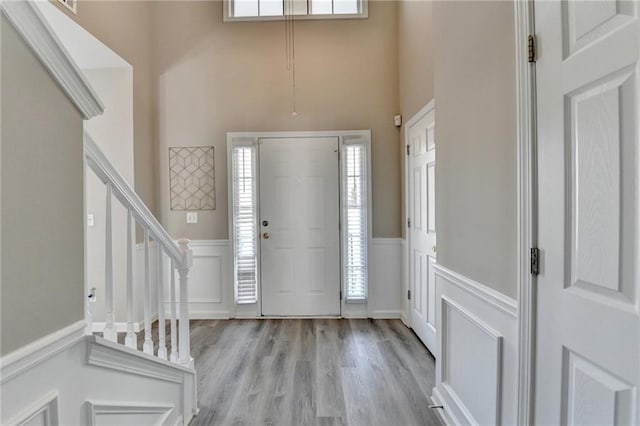 foyer with a decorative wall, a wainscoted wall, a towering ceiling, stairway, and light wood-type flooring