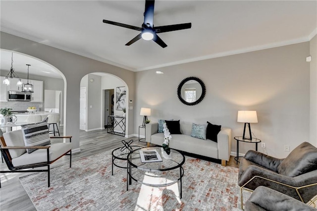 living area with light wood-type flooring, baseboards, arched walkways, and crown molding