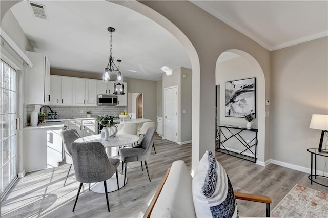 dining space with light wood-type flooring, visible vents, arched walkways, and baseboards