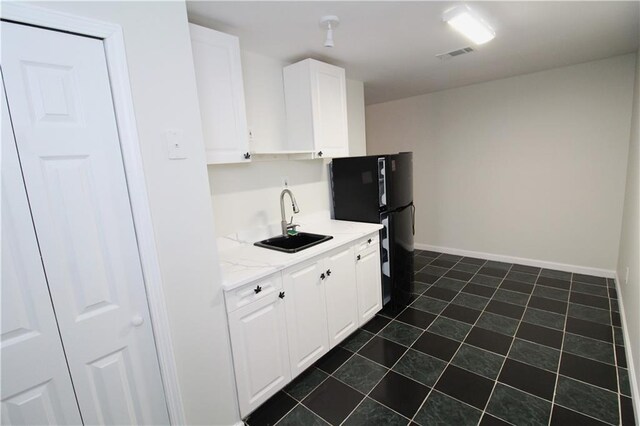 kitchen featuring white cabinetry, sink, dark tile patterned flooring, black fridge, and light stone countertops