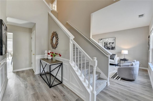 stairway featuring visible vents, a towering ceiling, baseboards, and wood finished floors