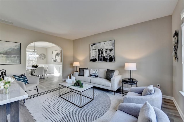 living room with baseboards, arched walkways, a chandelier, and wood finished floors