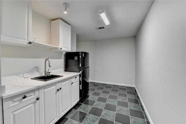 kitchen with baseboards, visible vents, white cabinets, freestanding refrigerator, and a sink