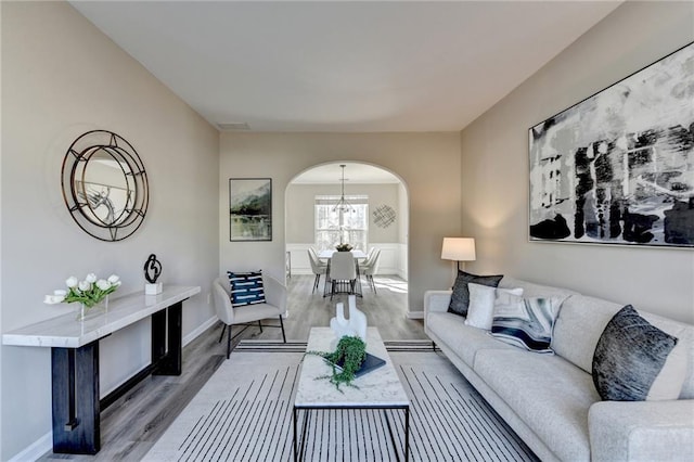 living area with baseboards, visible vents, arched walkways, wood finished floors, and a notable chandelier