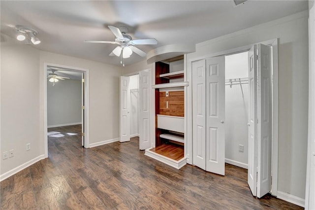 unfurnished bedroom with multiple closets, ceiling fan, baseboards, and dark wood-style floors