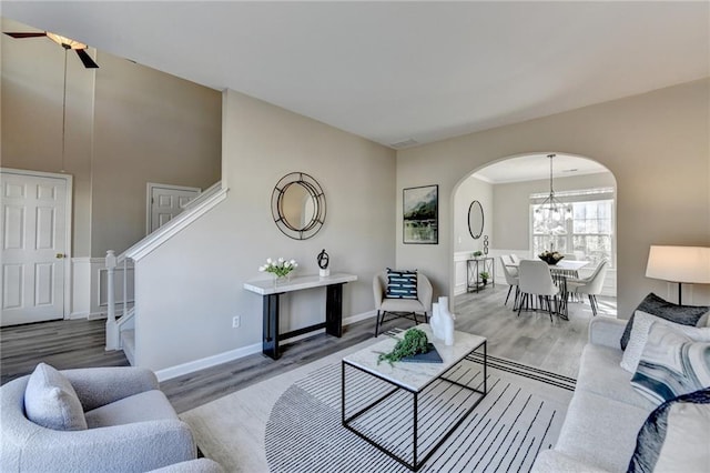 living room with stairs, arched walkways, wood finished floors, baseboards, and ceiling fan with notable chandelier