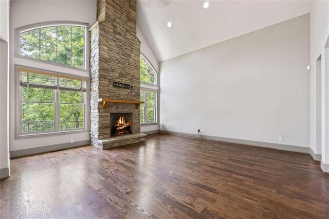 unfurnished living room with a stone fireplace, dark wood-type flooring, and high vaulted ceiling