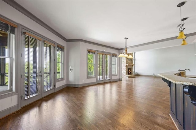 unfurnished dining area featuring crown molding, sink, a chandelier, dark hardwood / wood-style floors, and a stone fireplace