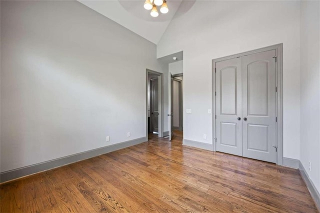 unfurnished bedroom with high vaulted ceiling and wood-type flooring