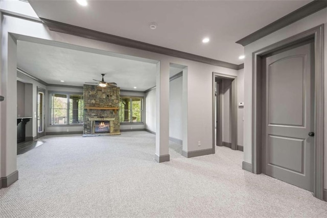 unfurnished living room featuring a stone fireplace, ceiling fan, crown molding, and light colored carpet