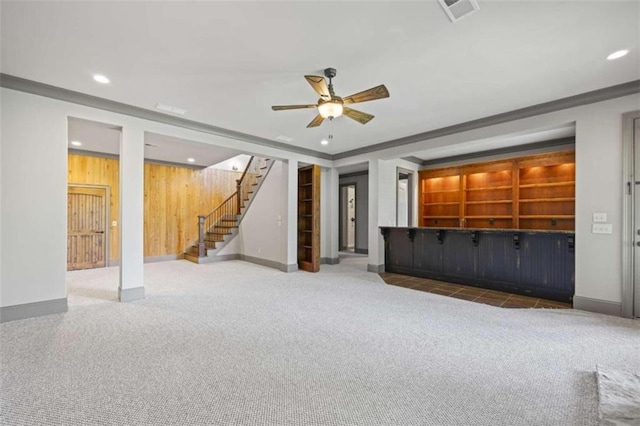 unfurnished living room with ornamental molding, carpet floors, ceiling fan, and wooden walls