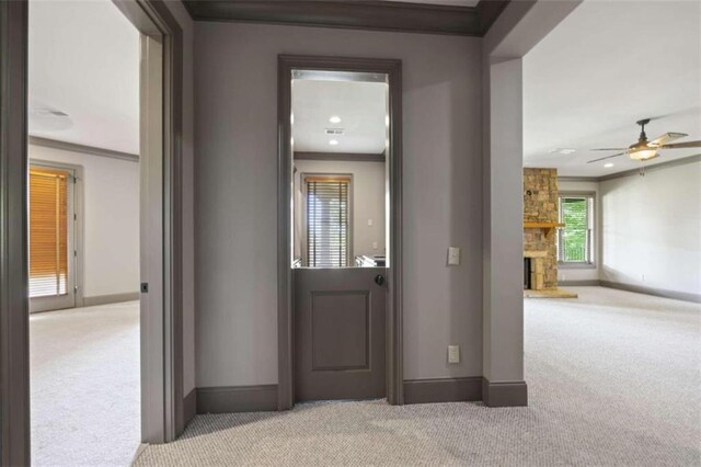 interior space featuring a stone fireplace, ceiling fan, light colored carpet, and ornamental molding