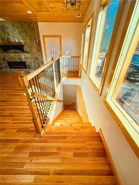 stairway with a stone fireplace, wooden ceiling, light hardwood / wood-style flooring, and a towering ceiling