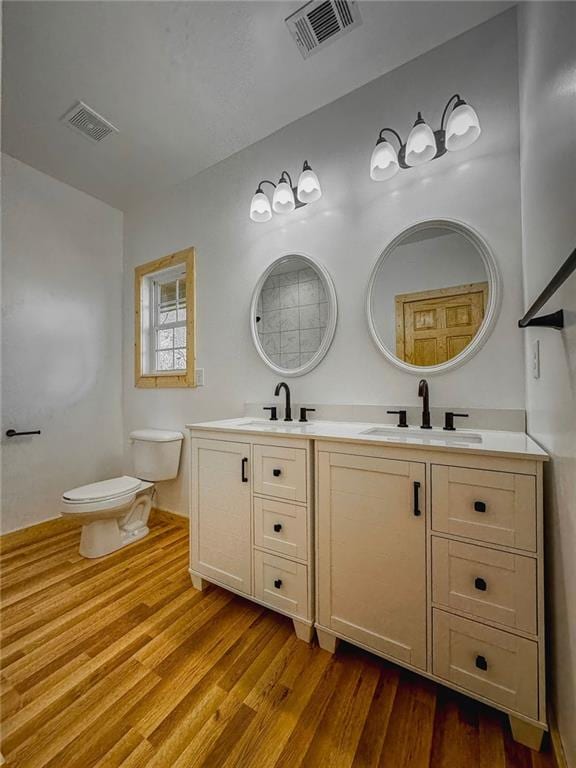 bathroom featuring toilet, wood-type flooring, and dual bowl vanity