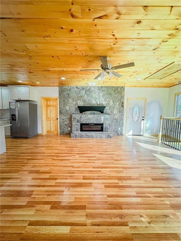 unfurnished living room with wood ceiling, a stone fireplace, ceiling fan, and light hardwood / wood-style floors