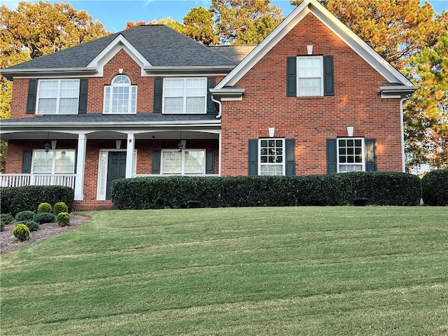 view of front of property with roof with shingles, a front yard, a porch, and brick siding