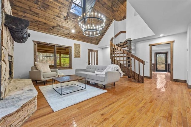 living room with high vaulted ceiling, an inviting chandelier, a stone fireplace, and light hardwood / wood-style floors