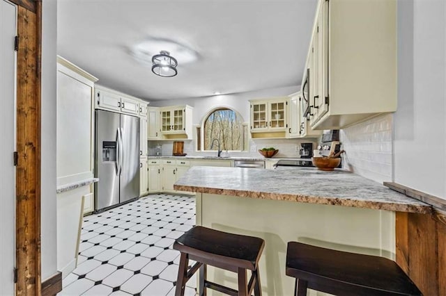 kitchen with decorative backsplash, sink, stainless steel fridge with ice dispenser, kitchen peninsula, and a breakfast bar area