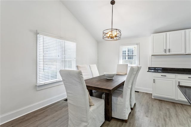 dining space with a notable chandelier, vaulted ceiling, and light wood-type flooring