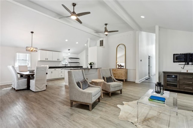 living room featuring ceiling fan with notable chandelier, lofted ceiling with beams, and light wood-type flooring