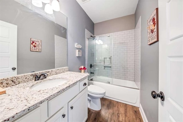 bathroom with vanity, toilet, wood finished floors, and bath / shower combo with glass door