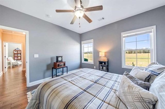 bedroom with wood finished floors, visible vents, baseboards, attic access, and ceiling fan